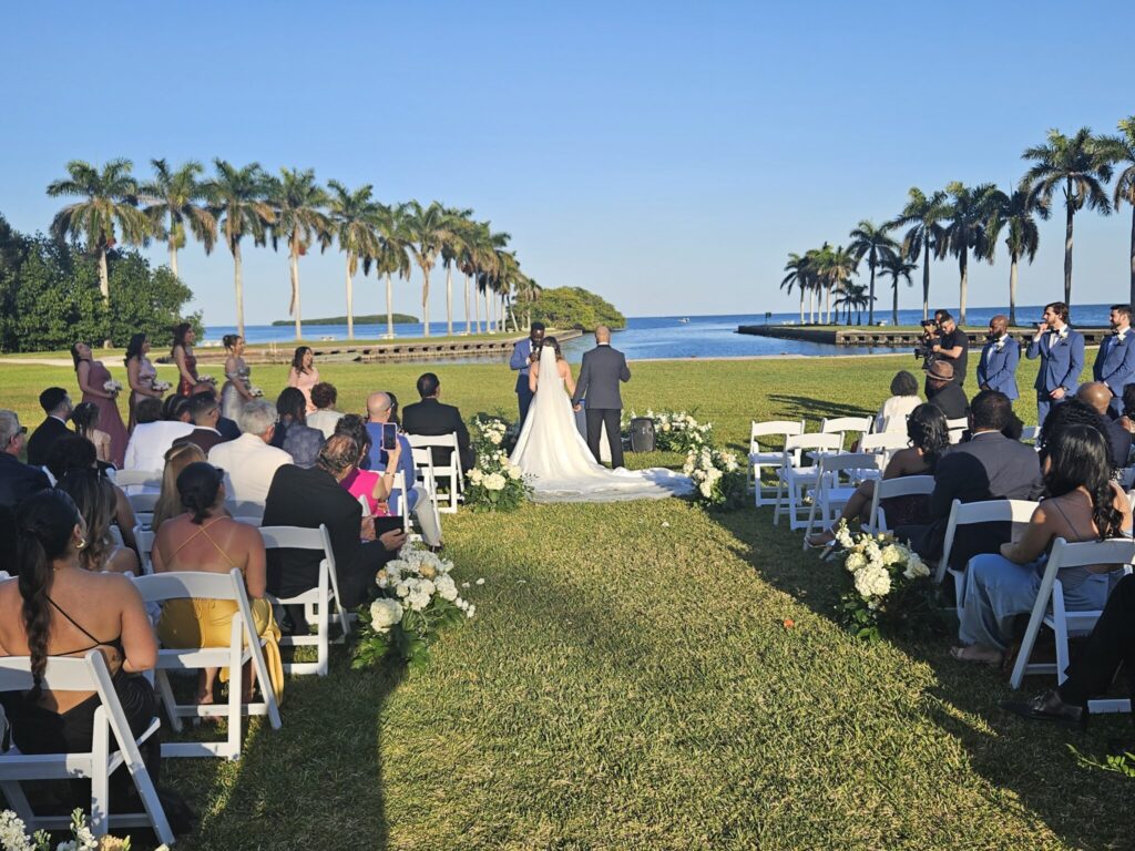 Outdoor waterfront wedding ceremony set up for wedding DJ services in Hollywood, FL on a oceanfront lawn lined with palm trees