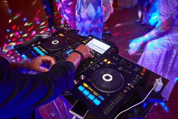 Professional event DJ mixing music on a digital Pioneer controller with vibrant disco lighting effects on a Hollywood, FL dance floor