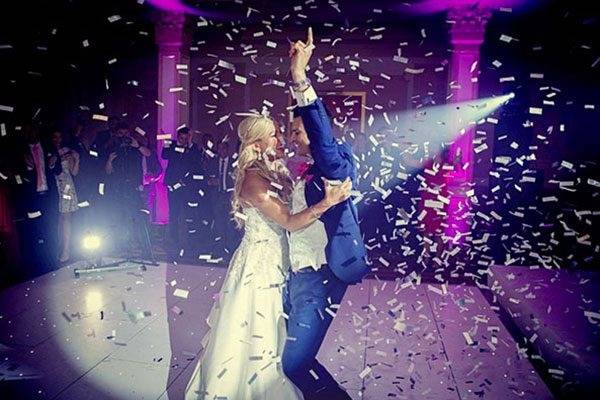 Wedding DJ celebration in Hollywood, FL featuring a bride and groom dancing on stage under falling confetti and purple spotlights