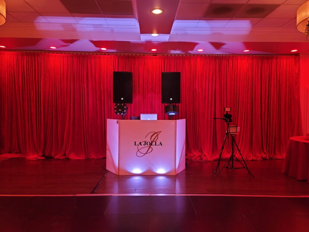 Professional DJ booth setup with sound speakers, red backdrop curtains, and lighting in Weston, FL