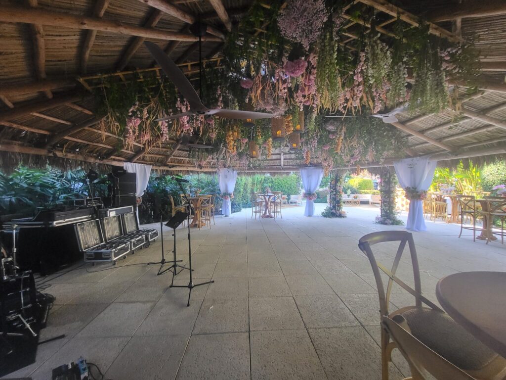Open-air tiki hut event space setup with hanging floral decor and sound gear in Fort Lauderdale, FL