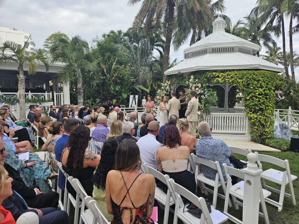 Outdoor garden wedding ceremony audio setup in Hollywood, FL with guests seated before a white gazebo surrounded by tropical greenery